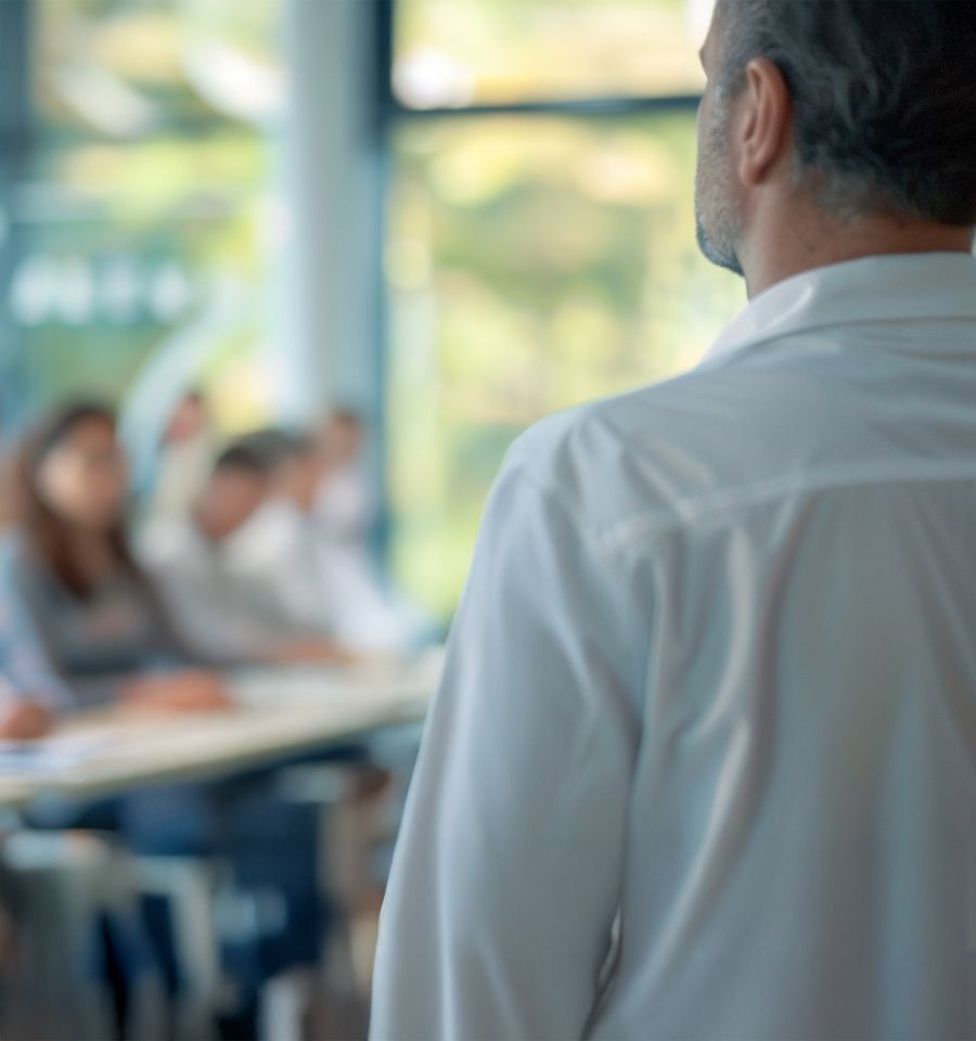 Ein Professor, der einen Vortrag hält - im Hintergrund verschwommen die Teilnehmer:innen